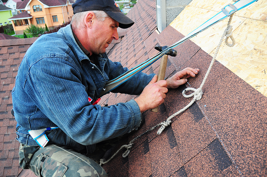 Roofer laying asphalt shingles. Roofer with safety kit on the house installing roof; roof installation