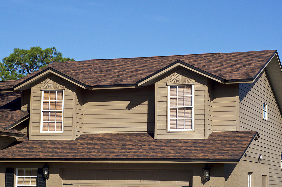 View of brown two story house against blue sky with gables windows and clean roof.
